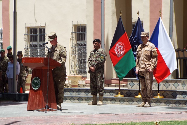 Záběr řečnického pultu. Kaplan HQ ISAF (Američan) zahajuje ceremonii. Za ním vlajka NATO a po jejich stranách vlajky národů, jejichž vojáci v uplynulém období padli (ČR a Afghánistán). U vlajek stojí národní představitelé, čekající na vyzvání k projevu (přednesení jmen).

 

